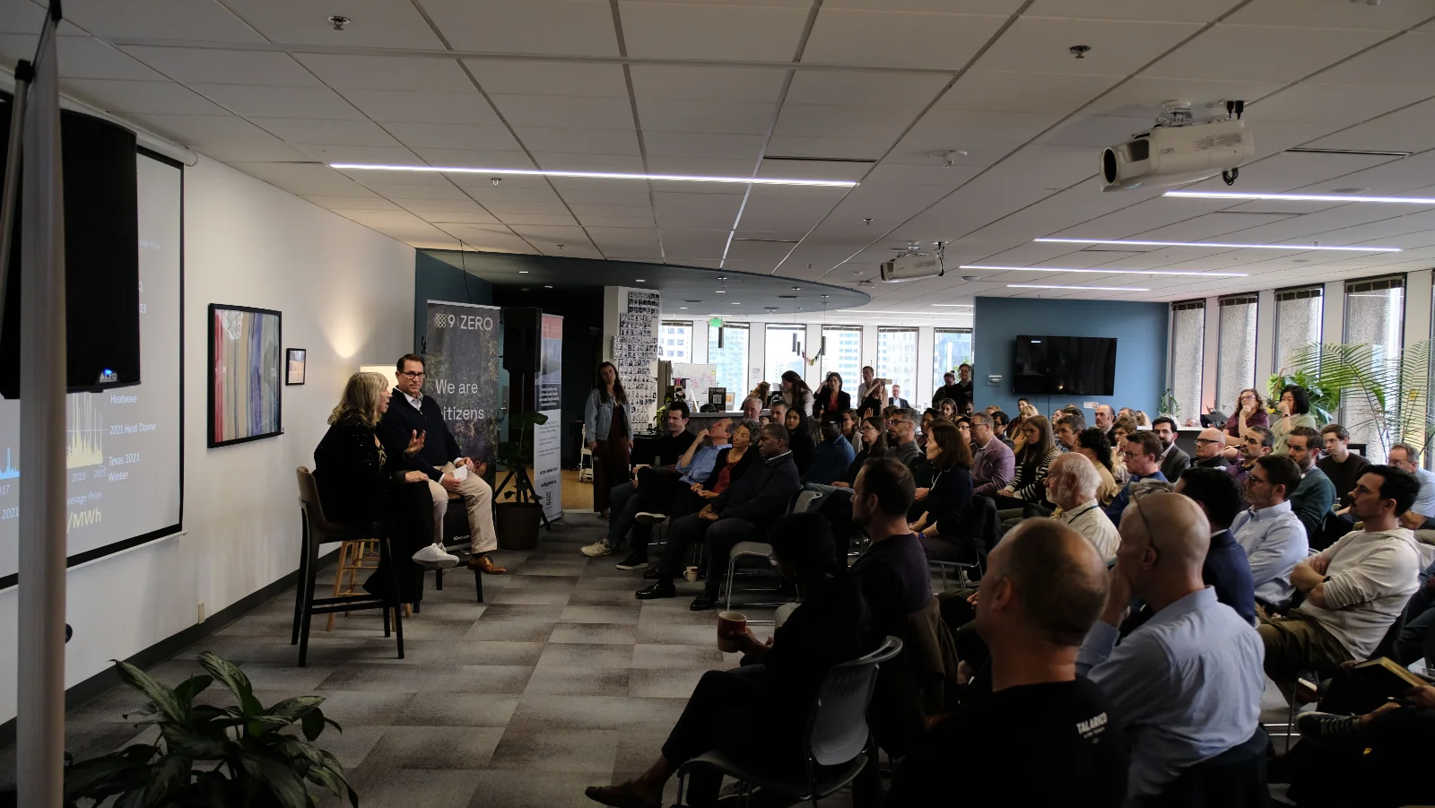 Dawn Lindell and Jeff Nichols seated on stage at the 9Zero Climate Innovation Hub in Seattle, facing a packed room of more than 100 attendees, with a power price chart projected on the screen beside them.