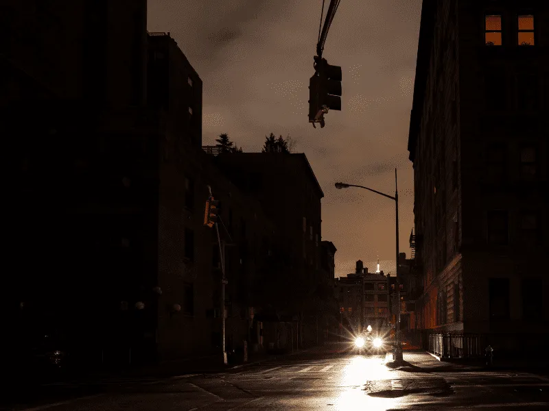 A dark city street during a power outage, lit only by a car's headlights